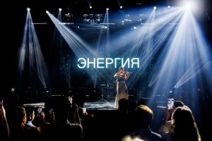 Открытие корпоративного мероприятия с ведущим на сцене и словом "ЭНЕРГИЯ" на большом экране.