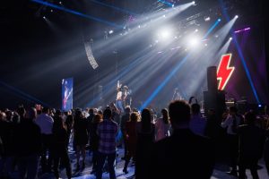 Сцена с мощным световым оборудованием и лучами прожекторов, оформленная в стиле рок-концерта.