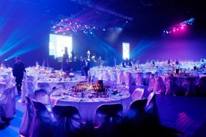 Общий план банкетного зала с накрытыми столами и сценой, подготовленного для масштабного корпоратива.